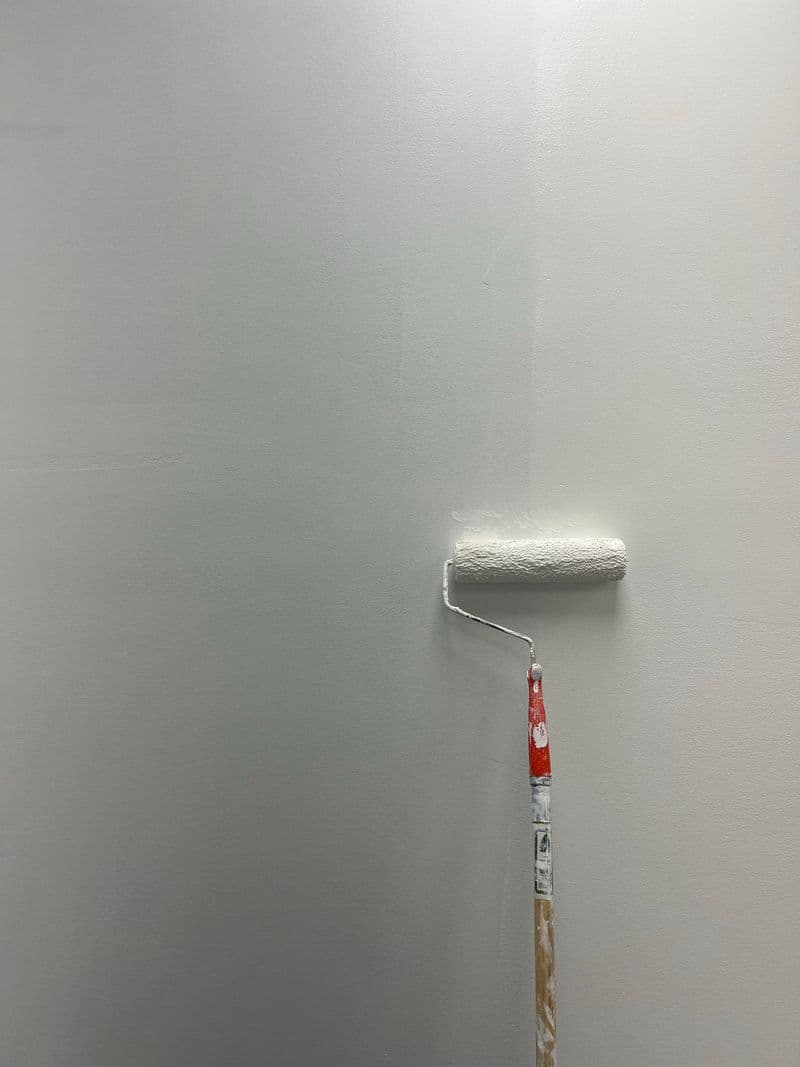 A roller applying a fresh coat of pale paint to a wall